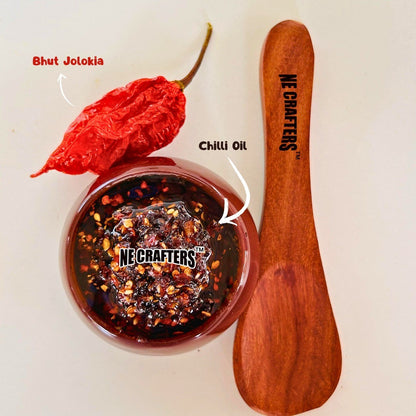 Bhut Jolokia chili pepper, NE Crafters chilli oil, and wooden spoon on a white background